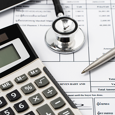 Calculator, stethoscope, and pen on medical invoice form assessing patient billing costs