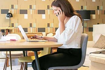 Young woman talking on phone and working on laptop at stylish living-room table