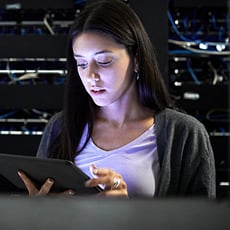Woman reviewing tablet while monitoring rack servers in dimly lit data center