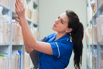 Nurse in blue uniform retrieving patient records from medical filing shelves