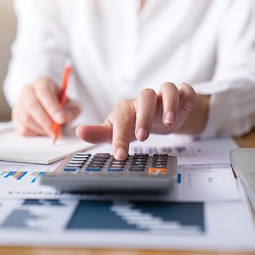 hand using a calculator on top of papers with data and graphs