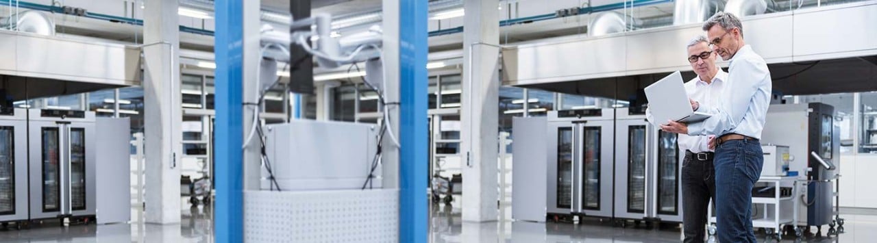 Two engineers reviewing laptop beside large automation equipment in clean manufacturing facility