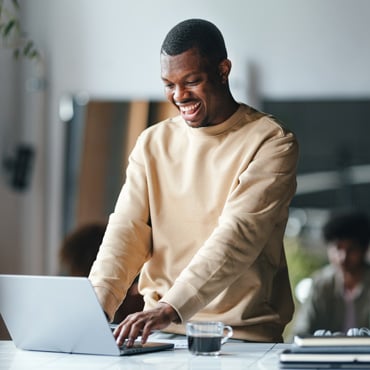 Smiling Black man standing at a desk and typing on a laptop while exploring employee retention strategies.