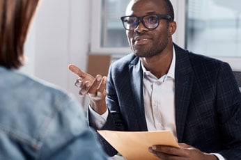Interviewer in suit and glasses gesturing while holding folder during meeting