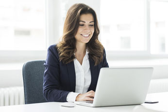 Smiling professional woman typing on laptop at bright modern office desk