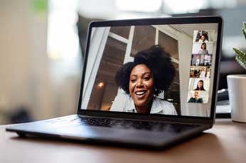Smiling woman leading a remote video meeting on laptop with visible participants