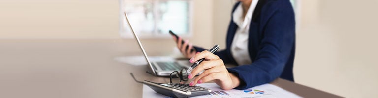 Person using calculator and smartphone while reviewing financial charts on desk