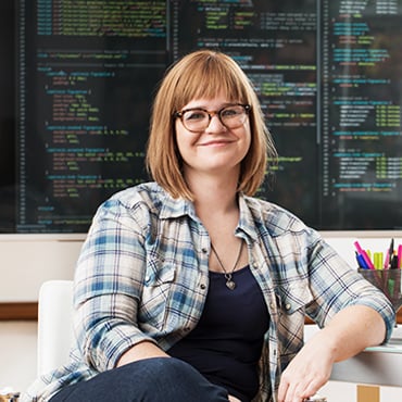 Smiling developer seated in front of monitors displaying source code