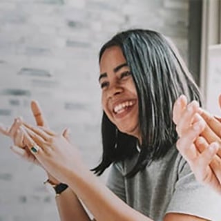 Young woman smiling and applauding while seated at a casual group gathering