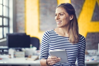 Young professional woman holding a tablet, smiling in a modern open-plan office
