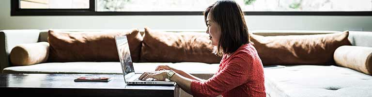 Young woman typing on laptop at low coffee table in bright living room