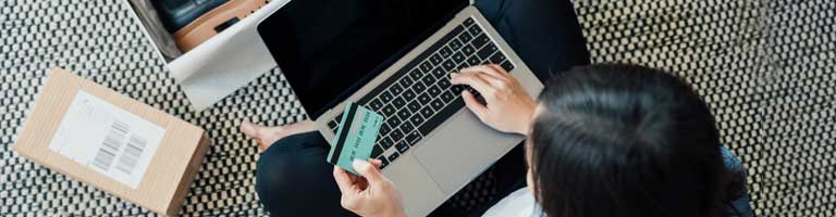 Person entering credit card details on laptop while packing a small shipping box