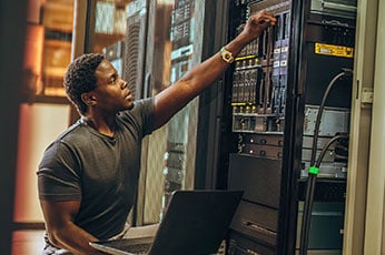 IT technician configuring rack-mounted servers in a data center with laptop