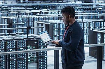 IT engineer checking laptop while monitoring server racks in data center