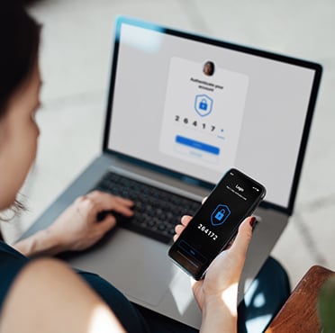 Person verifying code "264172" on phone while laptop shows two-factor prompt