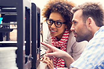 Two colleagues examining a 3D printer and discussing print details