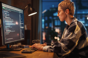 Software developer typing code on large monitor in evening office