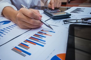 Hand using calculator while pointing at printed financial charts