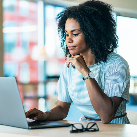 A professional woman wearing a light blue sweater learning AI skills on her laptop.