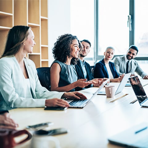 Smiling woman leading collaborative meeting at conference table with laptops and notes