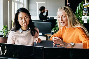 Two coworkers pointing at computer monitors while collaborating in office