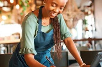 Small business owner smiling while organizing tasks after learning how to start a small business.