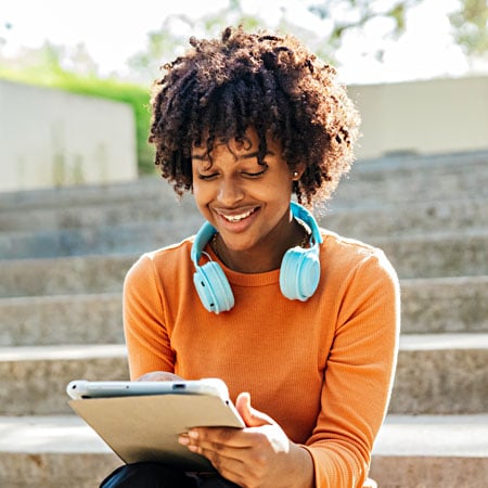 A woman wearing an orange shirt smiling as she works on a laptop.