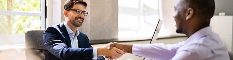 An HR professional and job candidate shaking hands in an office.