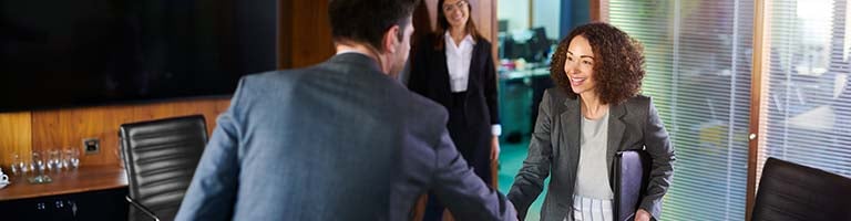 A job candidate cheerfully greeting her two interviewers in an office setting.
